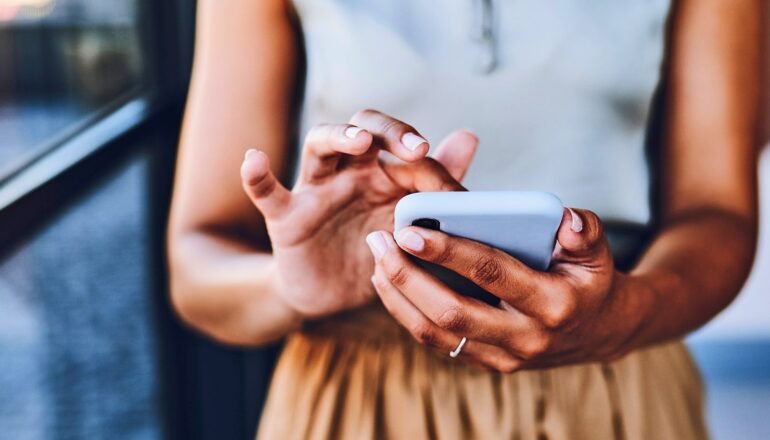 A woman scrolls through her phone while standing outside.