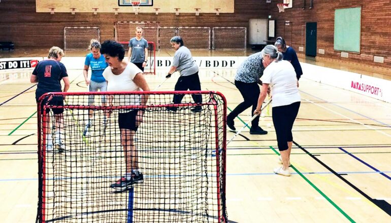 A group of women play floorball on a court in a gymnasium.