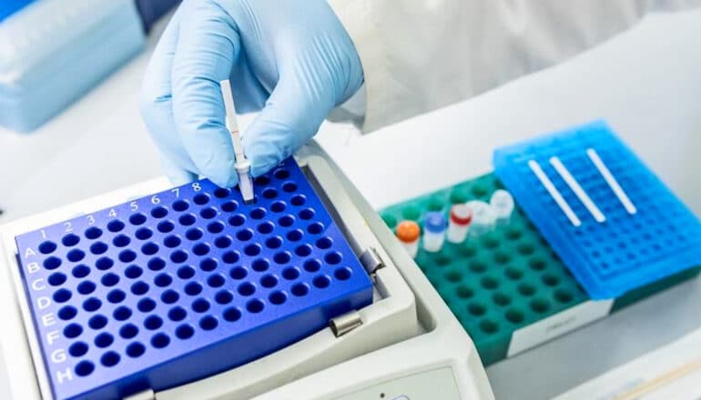 A gloved researcher places a sample into a testing device.