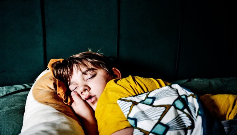 A young boy sleeps in a yellow t-shirt.