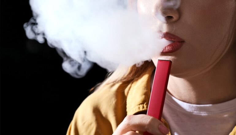A young woman exhales a cloud of vapor from her e-cigarette.