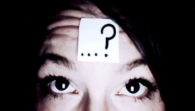 A woman has a post-it note with a question mark on her forehead.