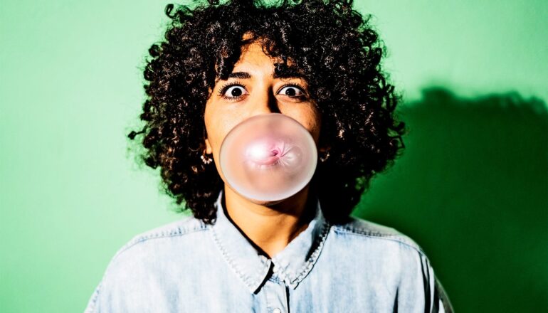 A woman looks alarmed as she blows a bubble with gum.
