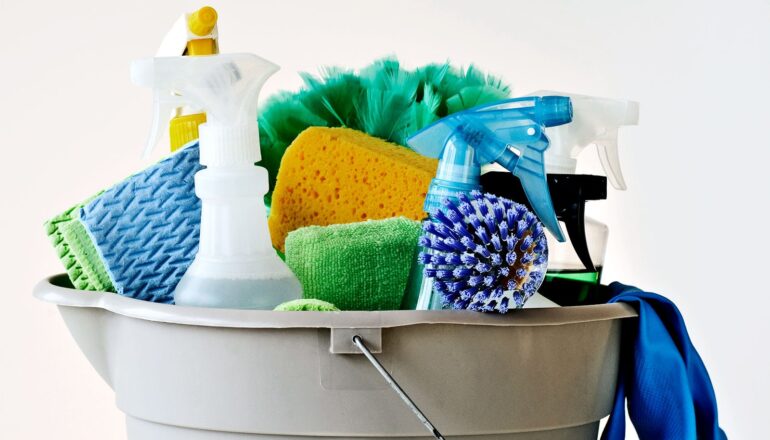 Cleaning product squeeze bottles and brushes sit in a bucket in front of a white background.