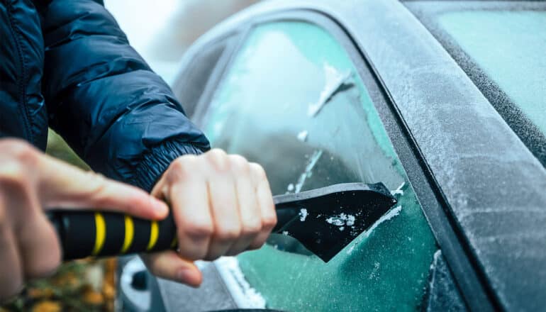 A person scrapes ice off of their car window.