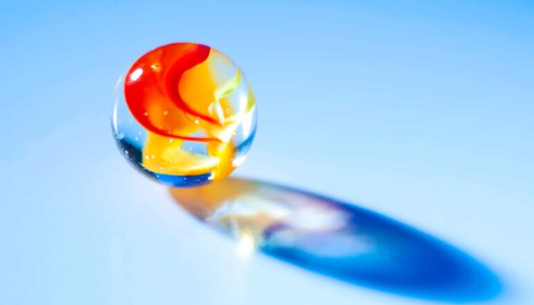 A marble with yellow and red swirls in it has light shining through it.