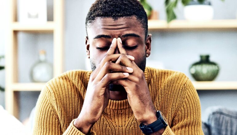 A man looks stressed and covers his face while sitting at a table.