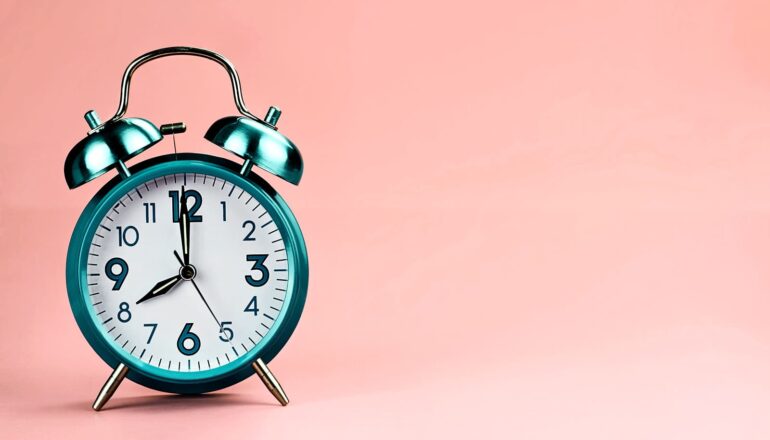 A green alarm clock in front of a pink background.