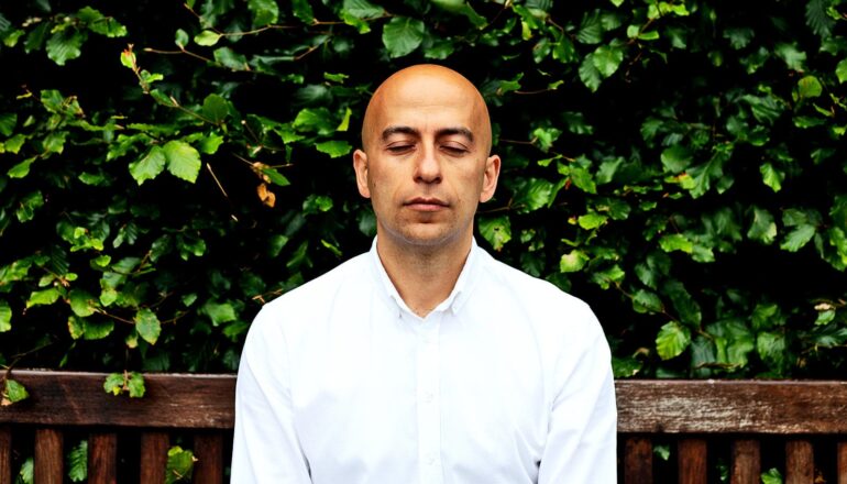 A man sits on a bench while closing his eyes.