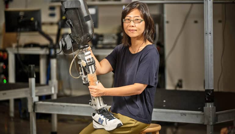 Helen Huang holds a robotic prosthetic leg while seated.