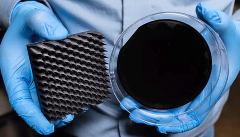A researcher holds up two pieces of the superblack material, which are incredibly dark.