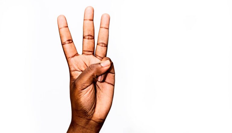 A person holds up three fingers against a white background.