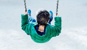 A young boy in a green jacket plays on a swingset.