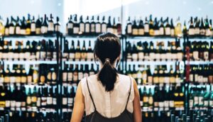 A woman stands in front of a store shelf filled with different bottles of wine.