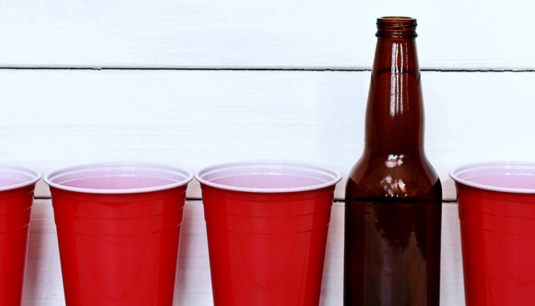 A row of red plastic cups with a beer bottle in between.