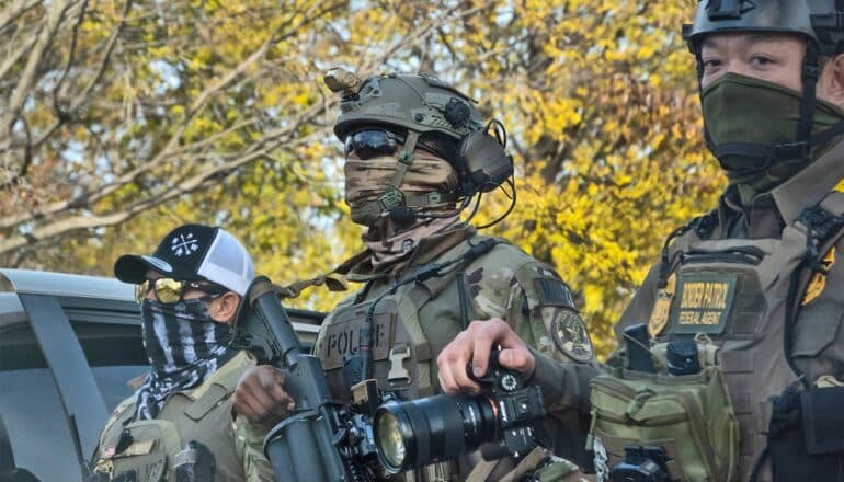 ICE officiers in tactical and camouflage gear, including face masks, stand in a row.