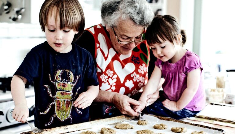 A grandmother makes cookies with her two grandchildren.