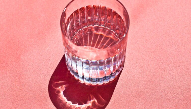 Light shines through a glass of water sitting on a pink surface.