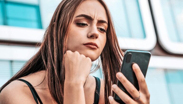 A woman looks skeptical as she reads her phone.