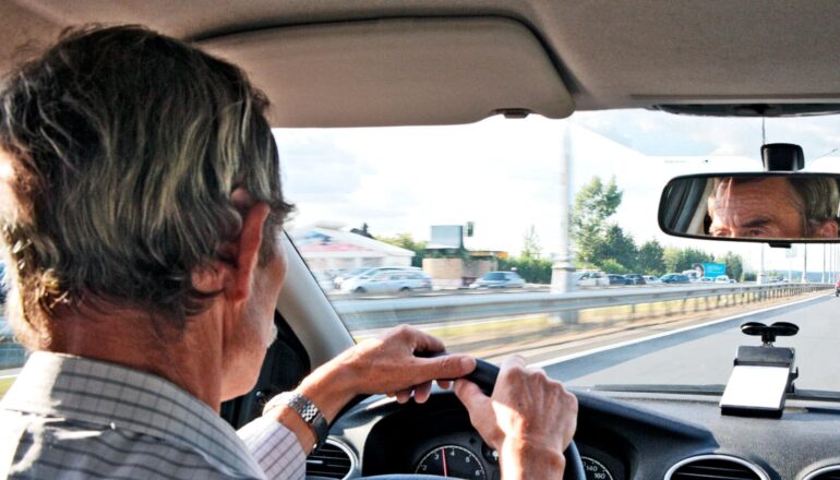 An older man behind the wheel of a car driving down the highway.