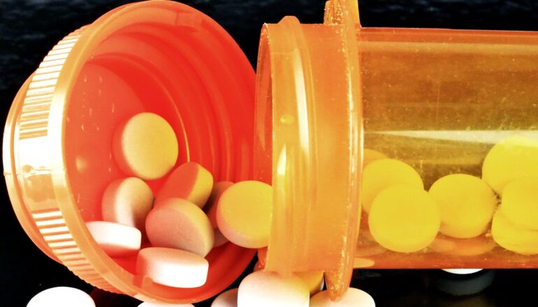 A pill bottle spills white pills onto a black surface.