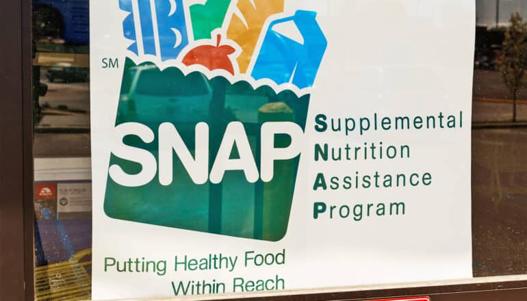 A sign that reads "SNAP: Supplemental Nutrition Assistance Program" in a store window.