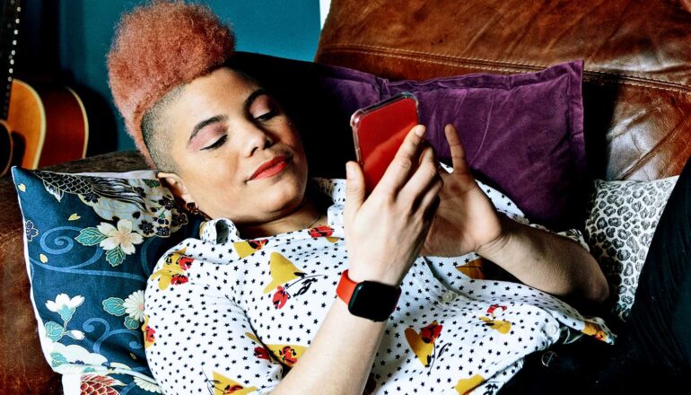 A woman leans back on a couch while scrolling on her phone.