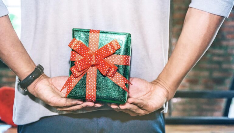 A man holds a gift-wrapped present behind his back.