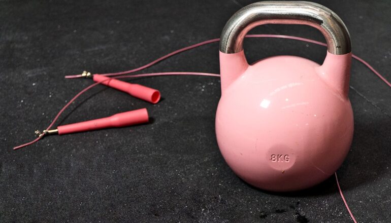 A jumprope and a kettlebell weight sit on a gym floor.