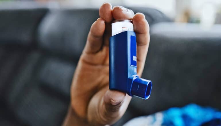 A person holds a blue asthma inhaler in one hand.