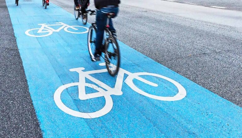 Cyclists ride bikes in a blue bike lane labeled with images of bicycles.