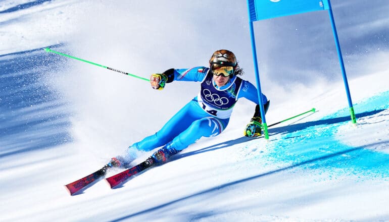 An Olympic skier curves around a flag while skiing downhill.