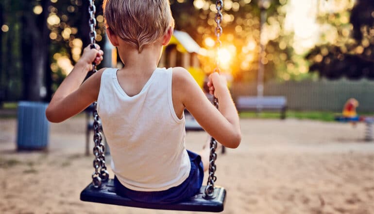 A young boy swings on a swing set in a park at sunset.