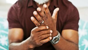 A man grasps his left hand with his right in pain.