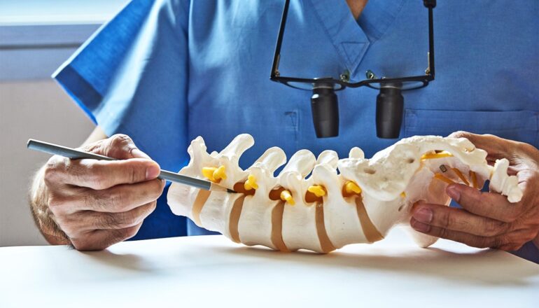 A doctor uses a pencil to point to a spine model while speaking with a patient.