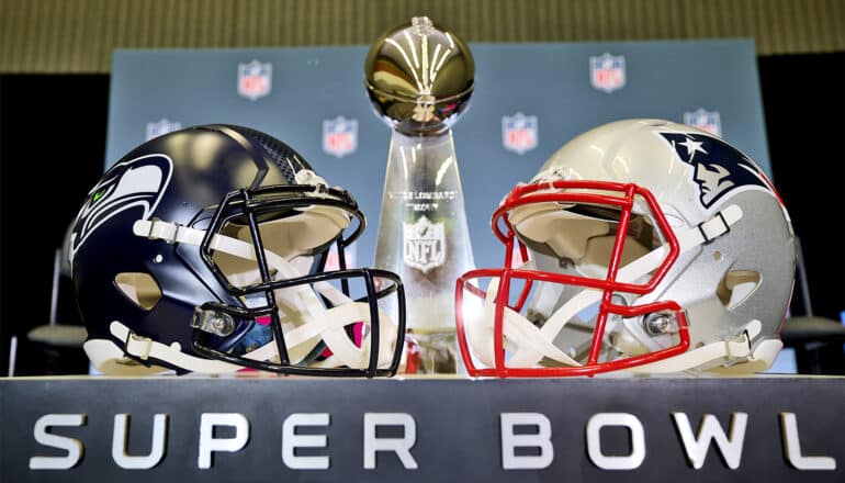 Two football helmets face each other with the Vince Lombardi Trophy placed between them.