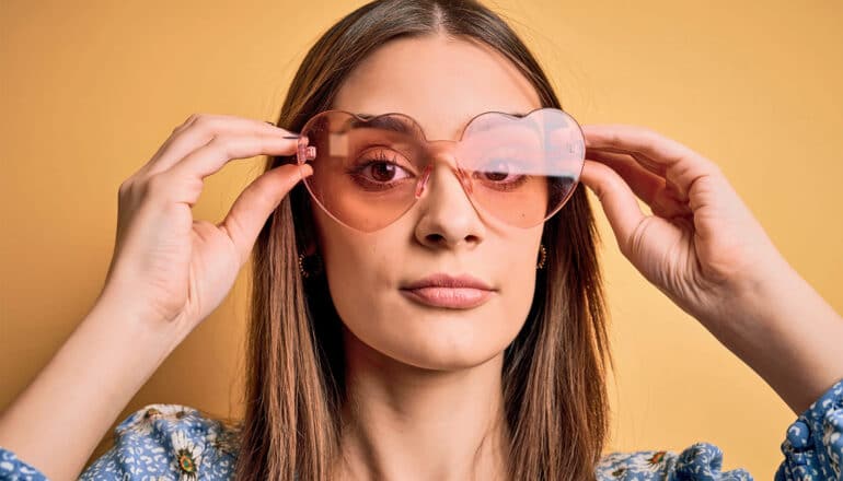 A young woman puts on pink heart-shaped glasses.