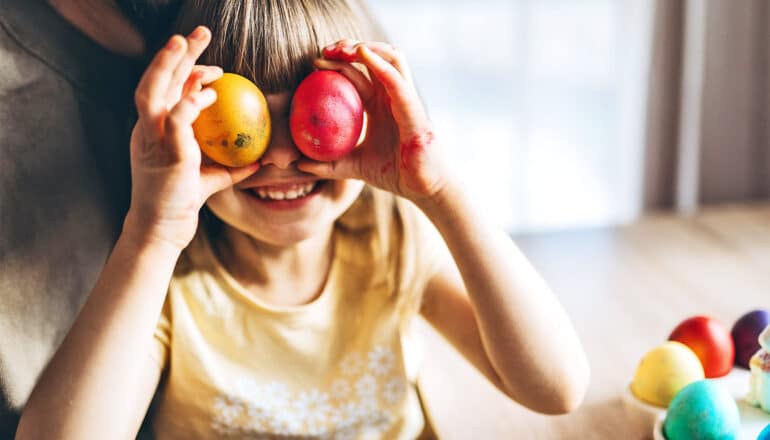 A young girl holds two dyed Easter eggs up to her eyes.
