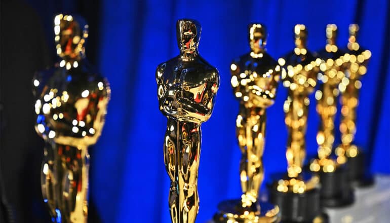 A row of golden Oscar statues in front of a blue curtain.