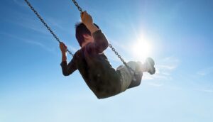 A young boy swings on a swing set in front of a bright blue sky.
