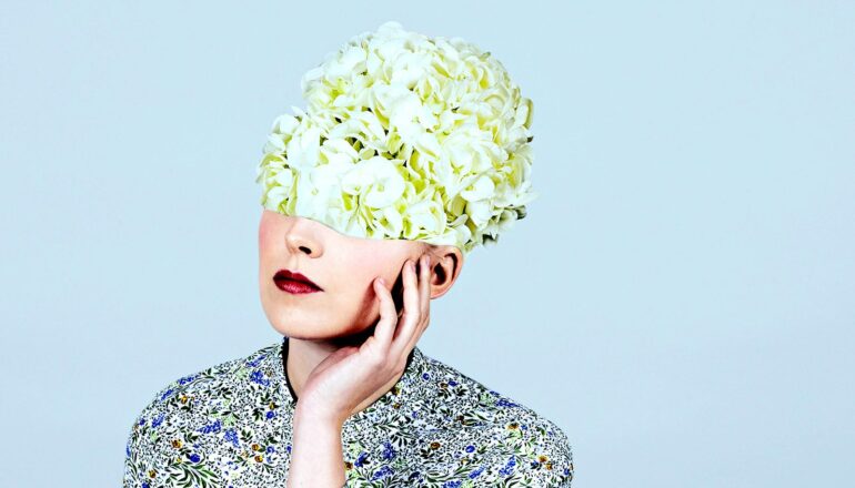 A woman touches her face as flowers bloom from her head.
