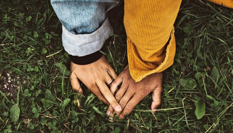 Two people touch hands while both sit on grass.
