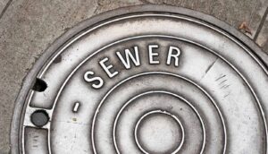 A city manhole cover has the word "sewer" on it.