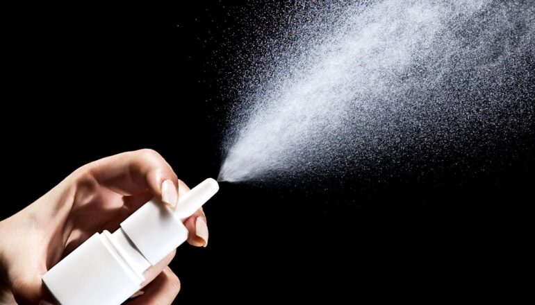 A person sprays mist from a small white nasal spray bottle.