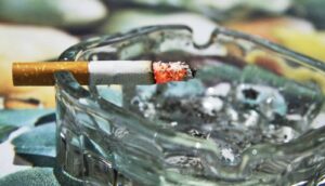 A lit cigarette sits in a glass ashtray.