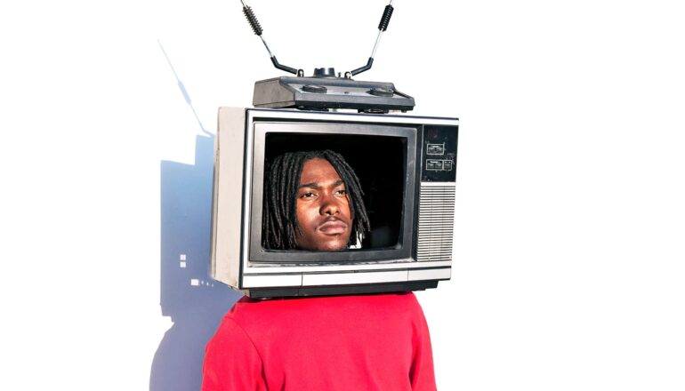 A man has an old TV on his head while standing in front of a white background.