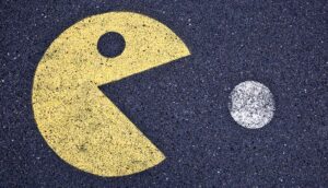 A painting of Pac Man eating a white circle on asphalt.