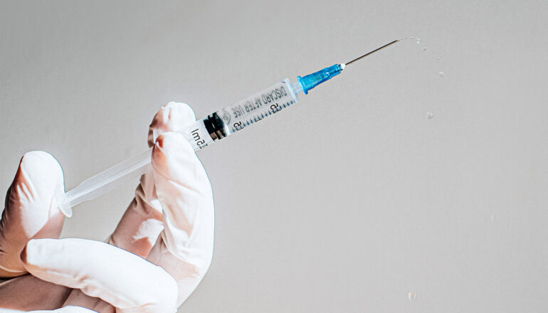 A person wearing a medical glove holds a syringe.