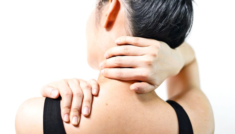 A woman clutches her shoulder and neck in pain.