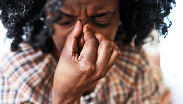 A woman holds the bridge of her nose in pain.